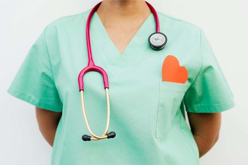 Nurse in light green scrubs with a red stethoscope around her neck.