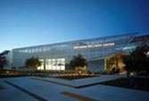 A modern glass building illuminated at dusk, surrounded by landscaped pathways and trees.